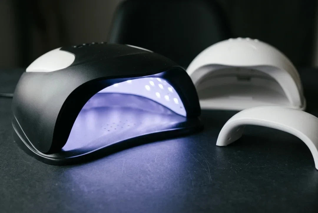 Trzy profesjonalne lampy UV/LED do paznokci na ciemnym blacie stanowiska, srodkowa wlaczona